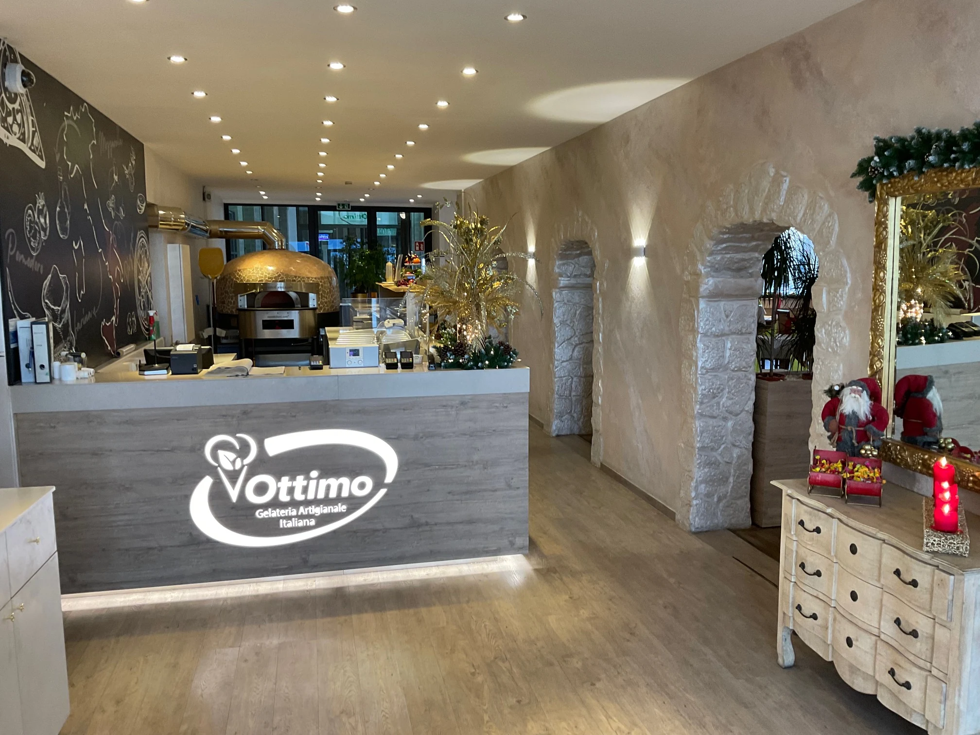 Pizzeria-Gastraum mit Theke in Holzoptik, goldenem Pizzaofen im Hintergrund und Natursteinbögen